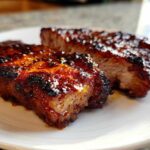 Close-up of two thick, caramelized pork steak pieces with a glossy, dark glaze on a white plate.