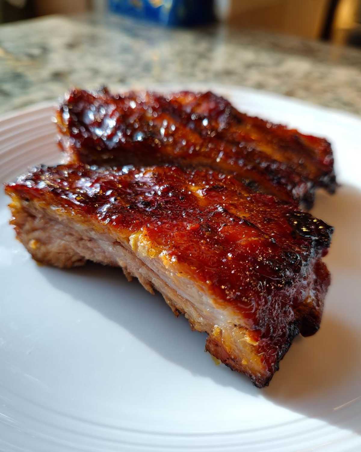 Close-up of two pieces of tender, glazed pork steak with a rich, dark red sauce on a white plate.
