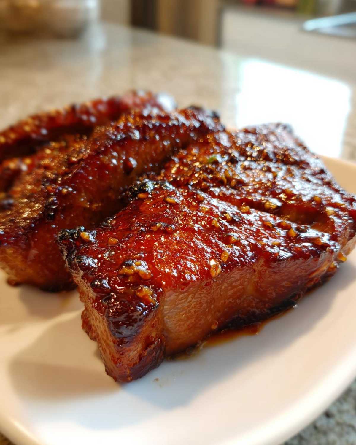 Close-up of two thick, glazed pork steak pieces coated in a sticky, dark sauce and sesame seeds.