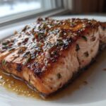 Close-up of a perfectly cooked salmon recipe fillet glazed with herbs and sauce on a white plate.