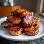 A close-up of thick slices of candied sweet potatoes stacked high, glistening with a rich, dark brown glaze.
