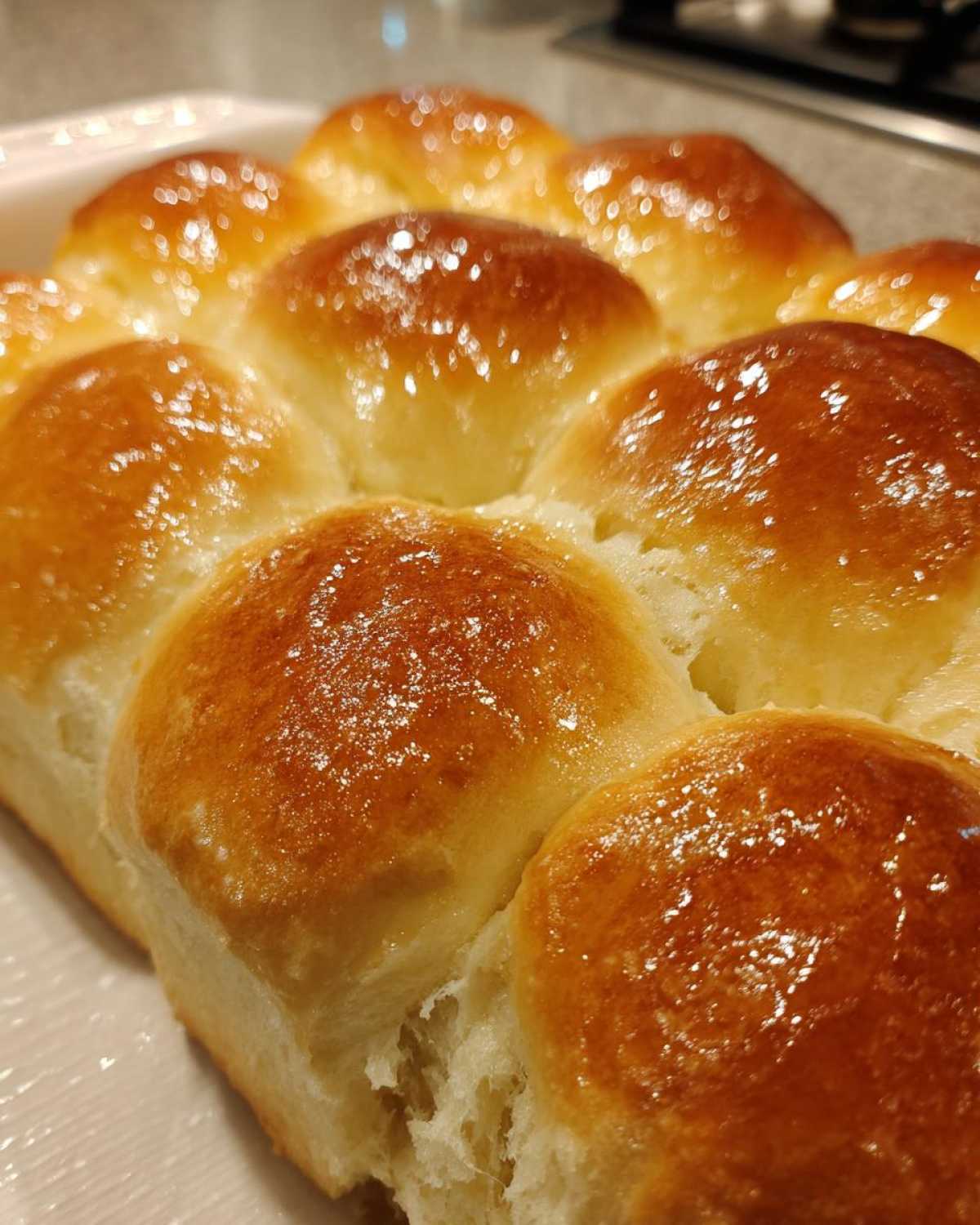 Close-up of soft, glossy sourdough discard rolls baked together in a white dish.