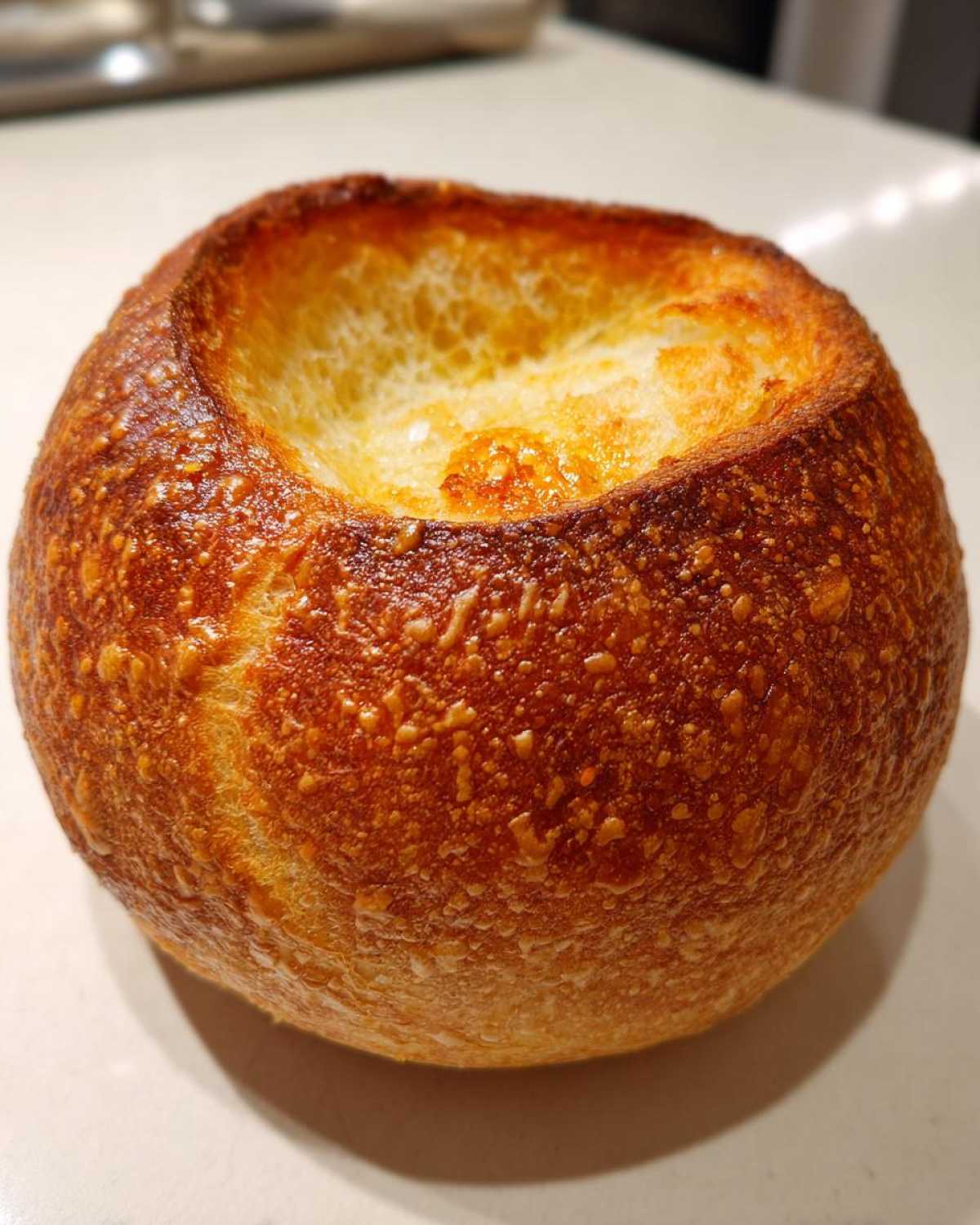 Close-up of a perfectly baked, round bread bowl with a deeply browned, blistered crust and hollowed top.