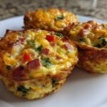 Close-up of three freshly baked Egg Muffin Cups filled with ham, cheese, and peppers on a white plate.