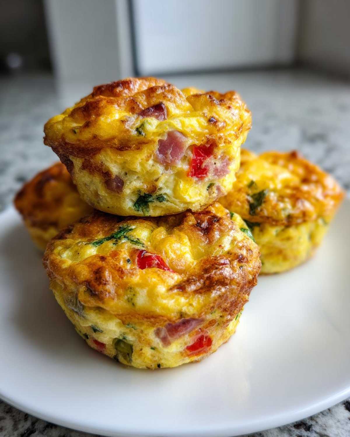 A stack of three golden brown Egg Muffin Cups filled with ham and peppers on a white plate.