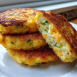 A stack of three golden brown mashed potato cakes, with one cut open showing cheese and chives inside.