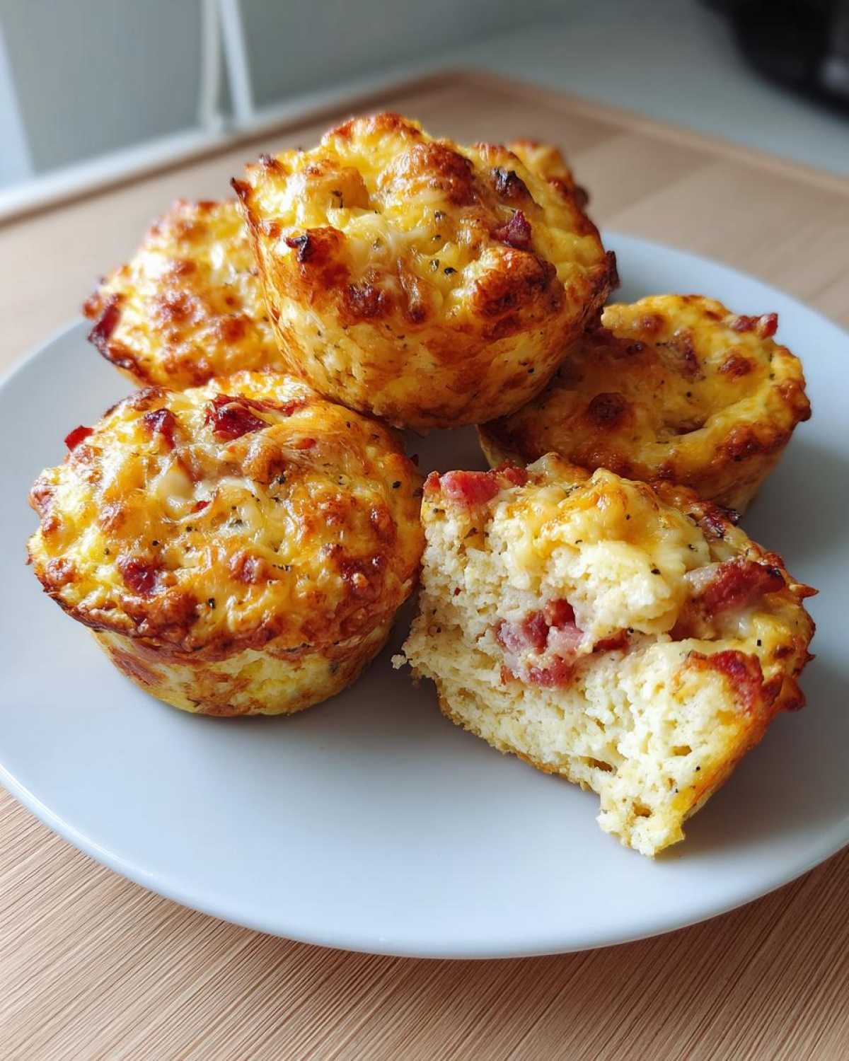 A close-up of several golden brown pizza muffins, one cut in half showing the cheesy interior with bits of meat.