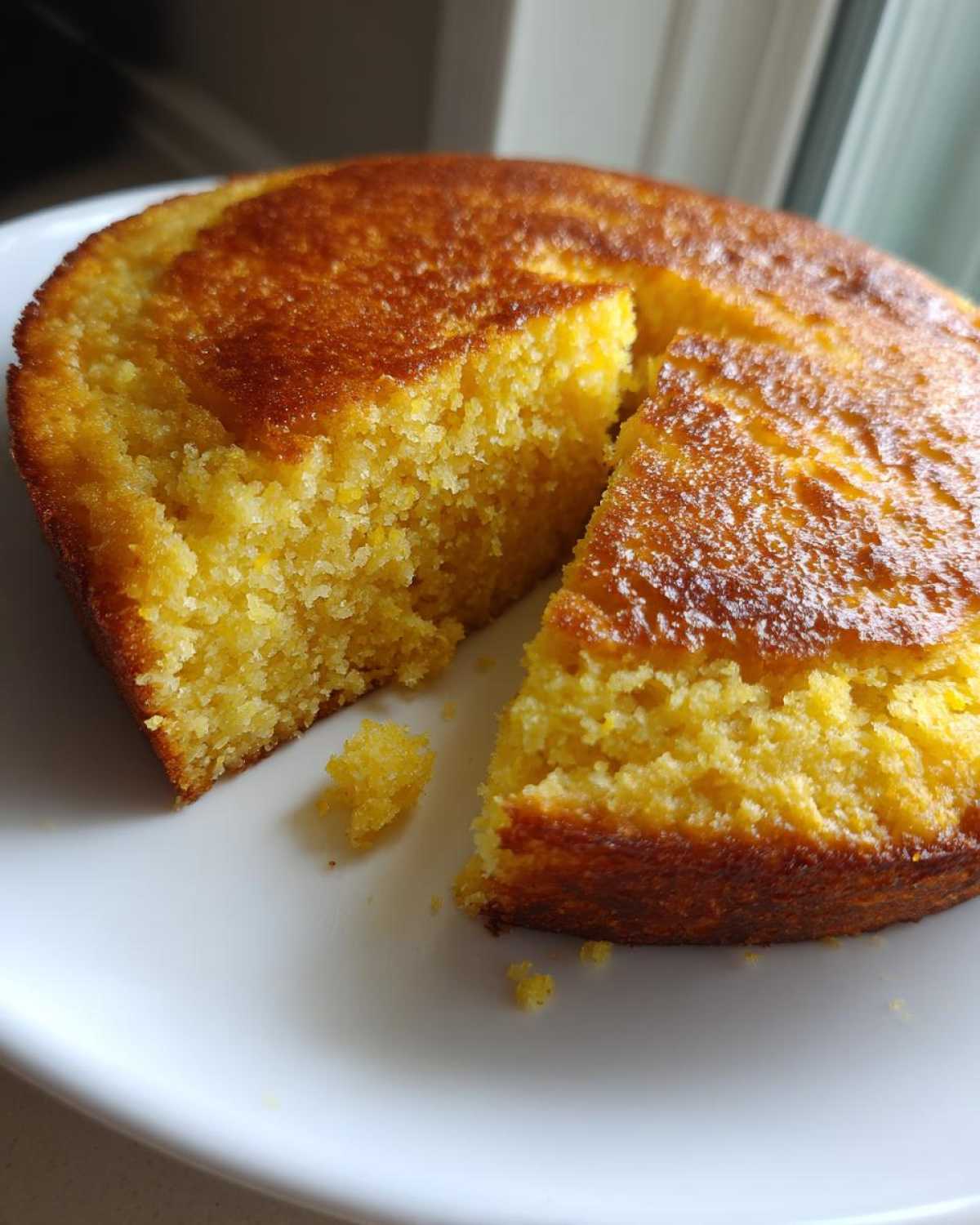 Close-up of golden brown skillet cornbread on a white plate with one slice cut out, showing the crumb texture.