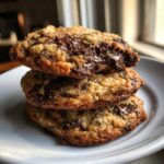 A stack of three gooey, golden-brown chocolate chip cookies with melted chocolate visible on top.