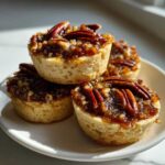 A stack of four gooey pecan pie cookies topped with caramelized pecans, sitting on a white plate.