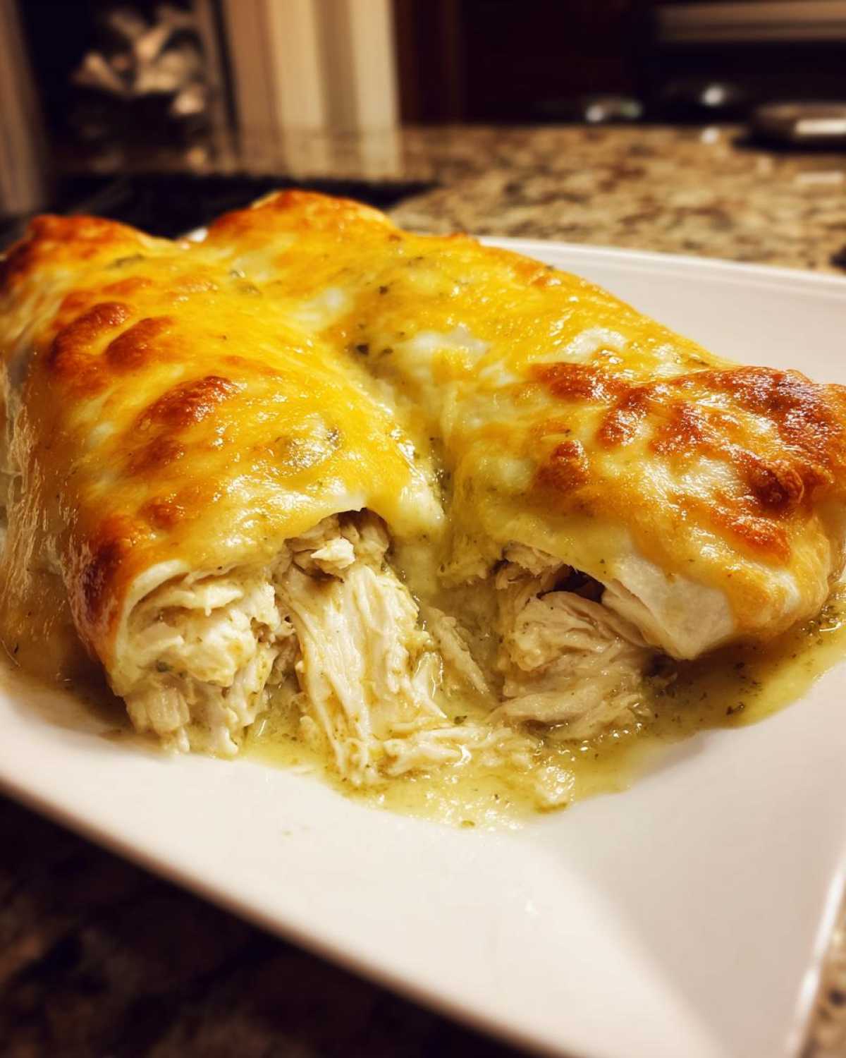 Close-up of two green chile chicken enchiladas smothered in melted, bubbly cheese.