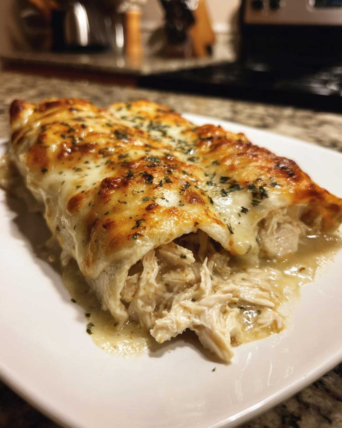 Close-up of green chile chicken enchiladas oozing shredded chicken and topped with melted, browned cheese and herbs.