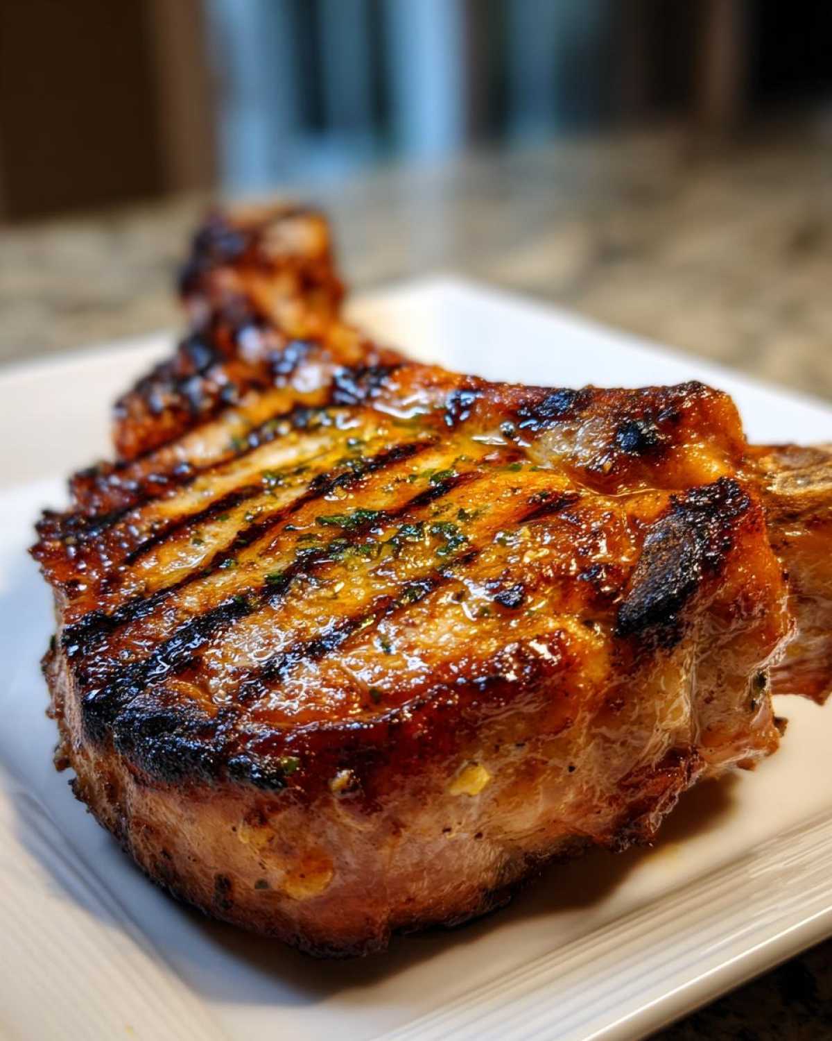 Close-up of a thick, juicy, grilled pork chop showing distinct grill marks and a glossy glaze, resulting from the marinade for pork chops.