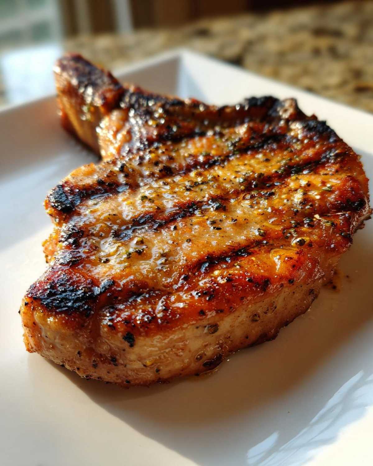 Close-up of a perfectly grilled pork chop showing char marks and a glossy marinade for pork chops.