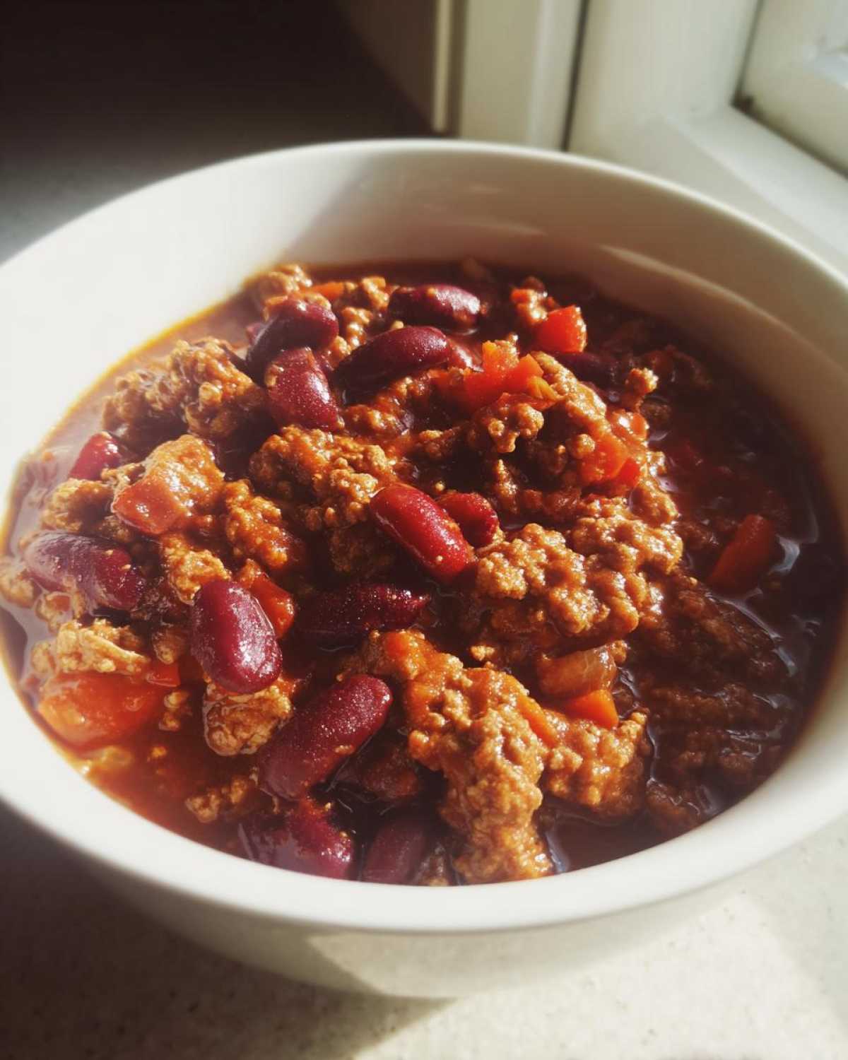 Close-up of a white bowl filled with rich, meaty crockpot chili featuring kidney beans and a thick tomato-based sauce.