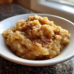A close-up of chunky homemade applesauce sprinkled with cinnamon, served in a white bowl.