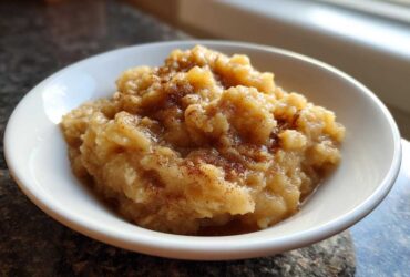 A close-up of chunky homemade applesauce sprinkled with cinnamon, served in a white bowl.