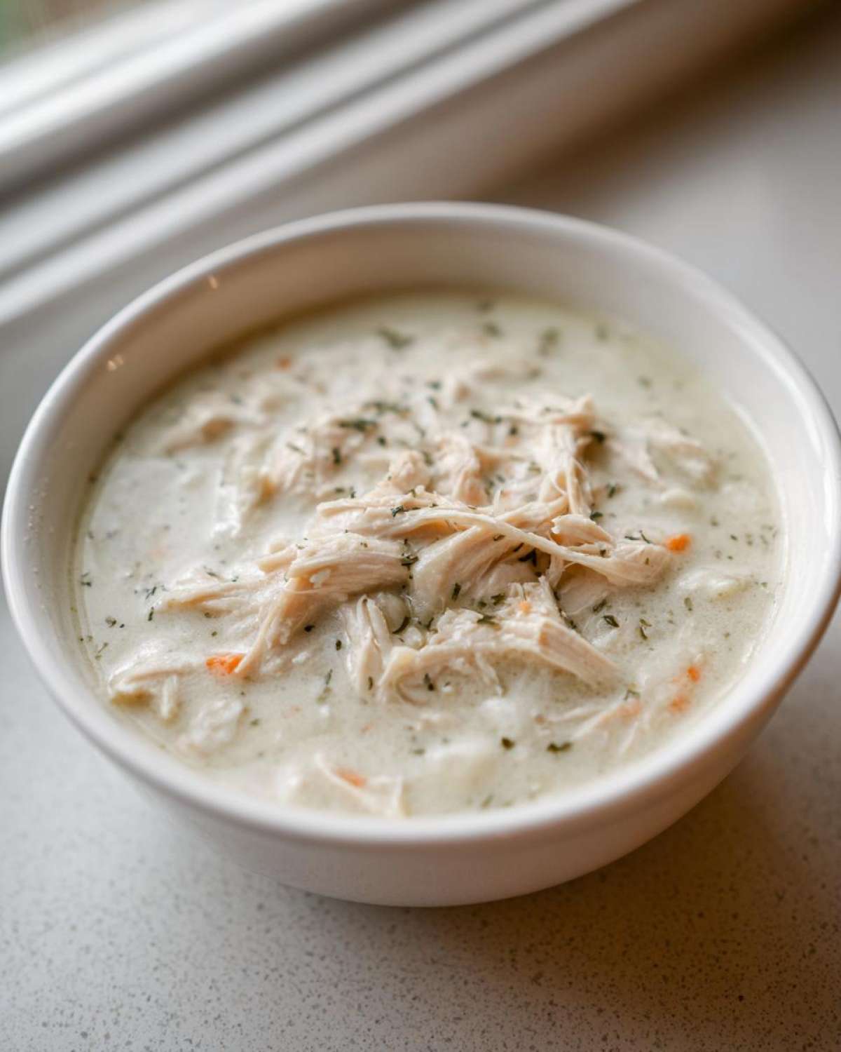 Close-up of a white bowl filled with rich homemade cream of chicken soup, topped with shredded chicken and herbs.
