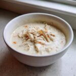A white bowl filled with rich homemade cream of chicken soup, topped generously with shredded chicken and small pieces of carrot.
