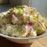 A close-up of creamy honey mustard chicken salad mixed with diced celery and red onion, served in a white bowl.