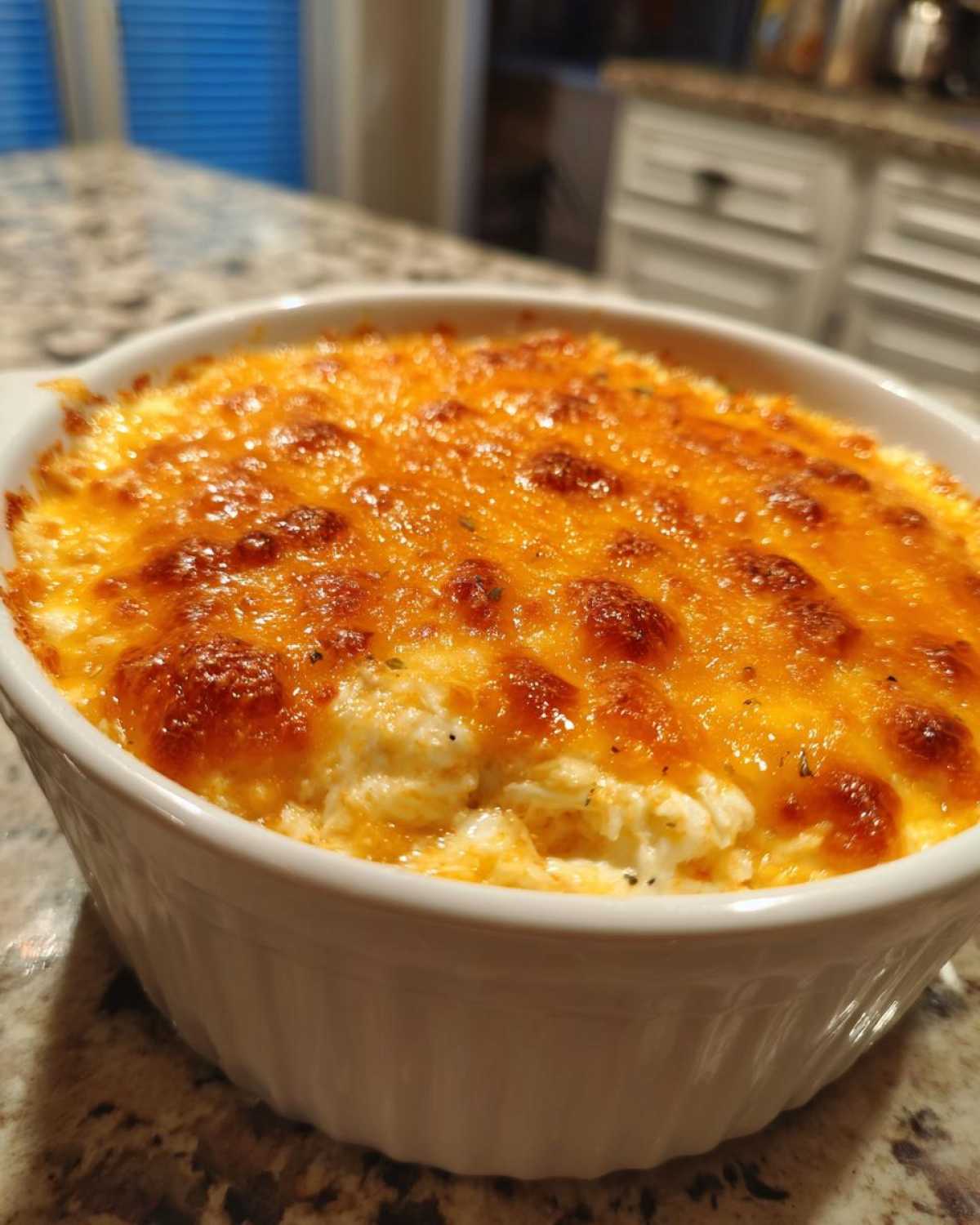 Close-up of a bubbling hot crab dip in a white ramekin, topped with melted, golden-brown cheese.