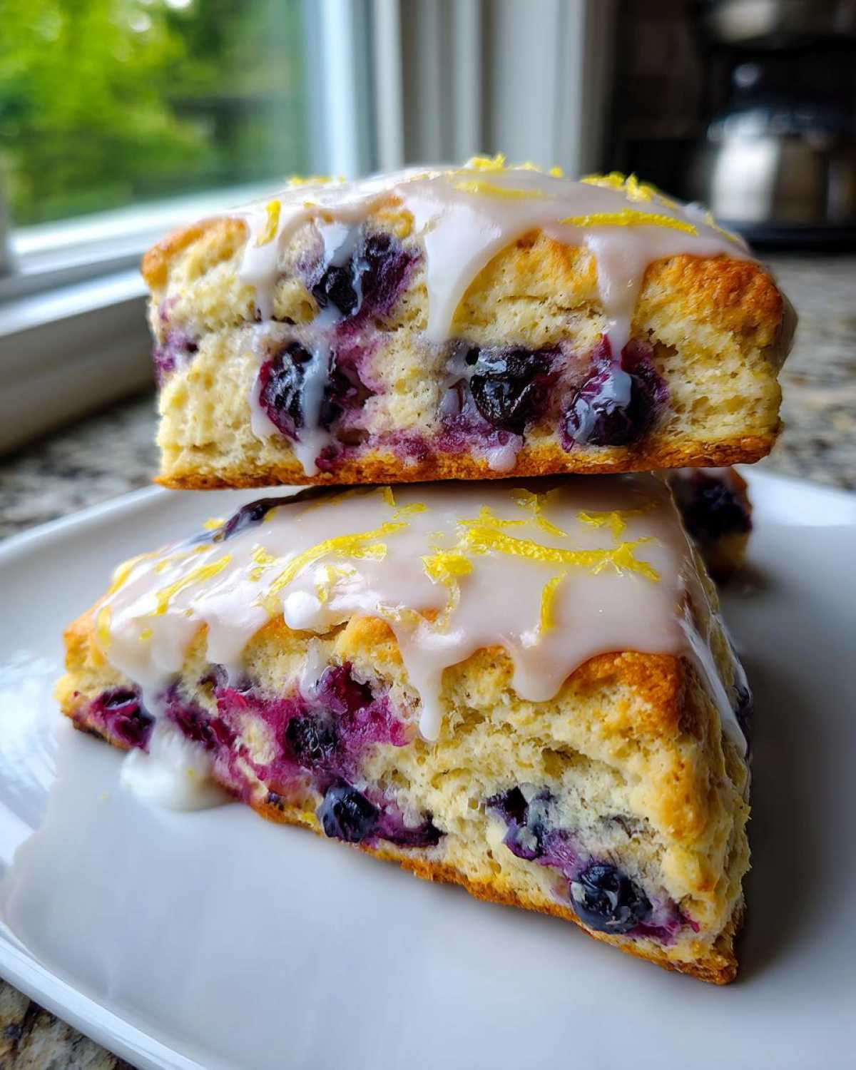 Two stacked, triangular blueberry scones topped with white lemon glaze and zest.