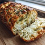 A golden-brown loaf of Italian herb and cheese bread, partially sliced to show melted cheese inside.