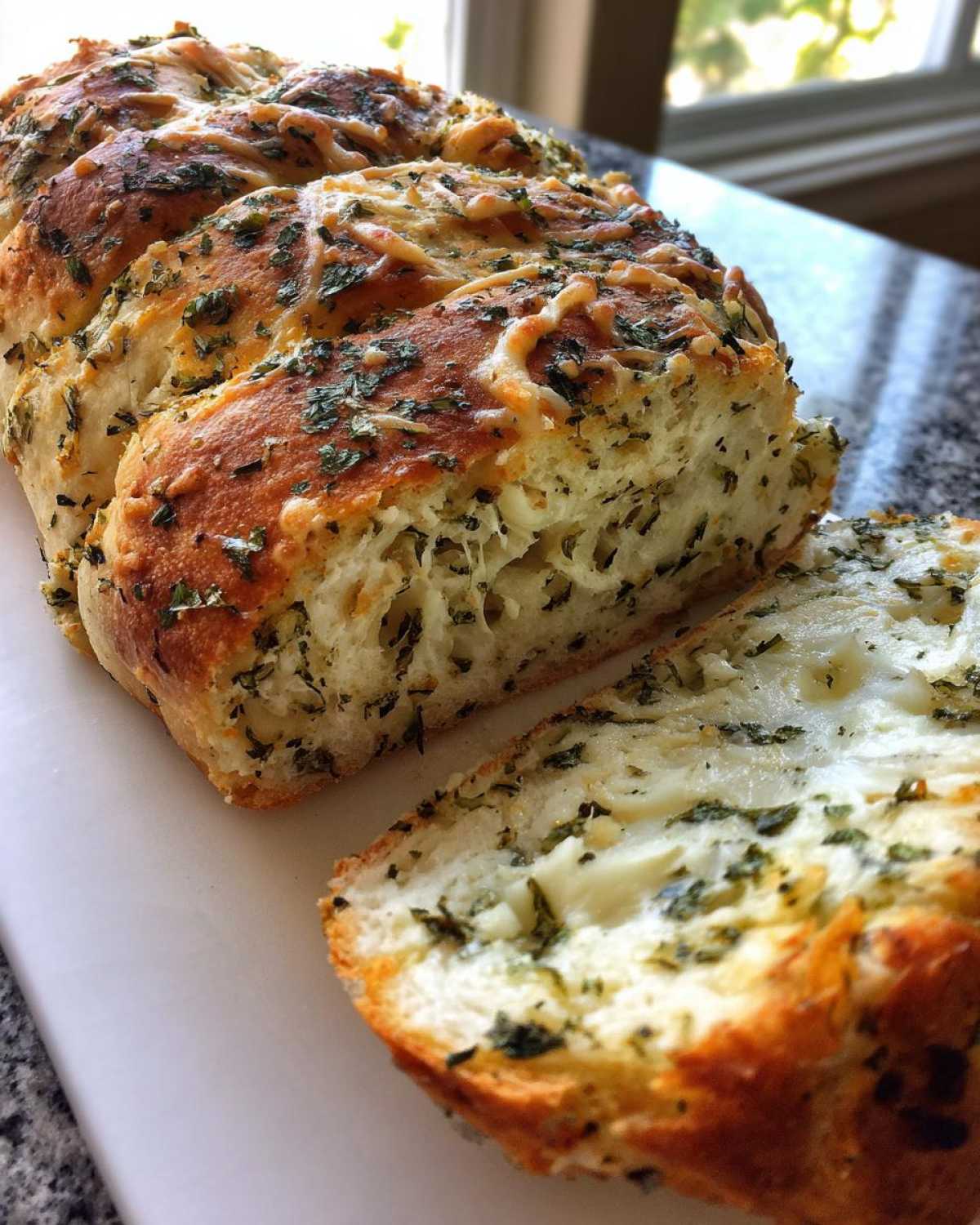 A loaf of golden brown Italian herb and cheese bread, partially sliced to show melted cheese and green herbs inside.
