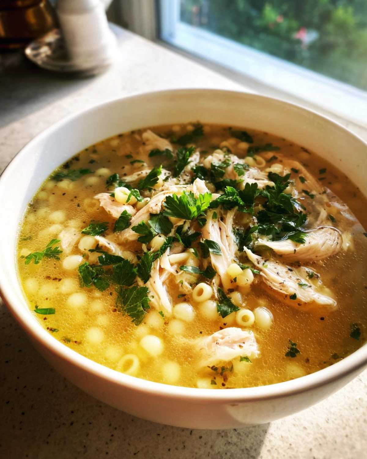 Close-up of a white bowl filled with Italian penicillin soup, featuring shredded chicken, small pasta, and fresh parsley garnish.
