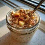 Close-up of apple cinnamon overnight oats in a glass jar, topped with diced apples and cinnamon.
