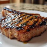 Close-up of a thick, grilled pork chop showing char marks and a glossy marinade glaze, ready to eat.