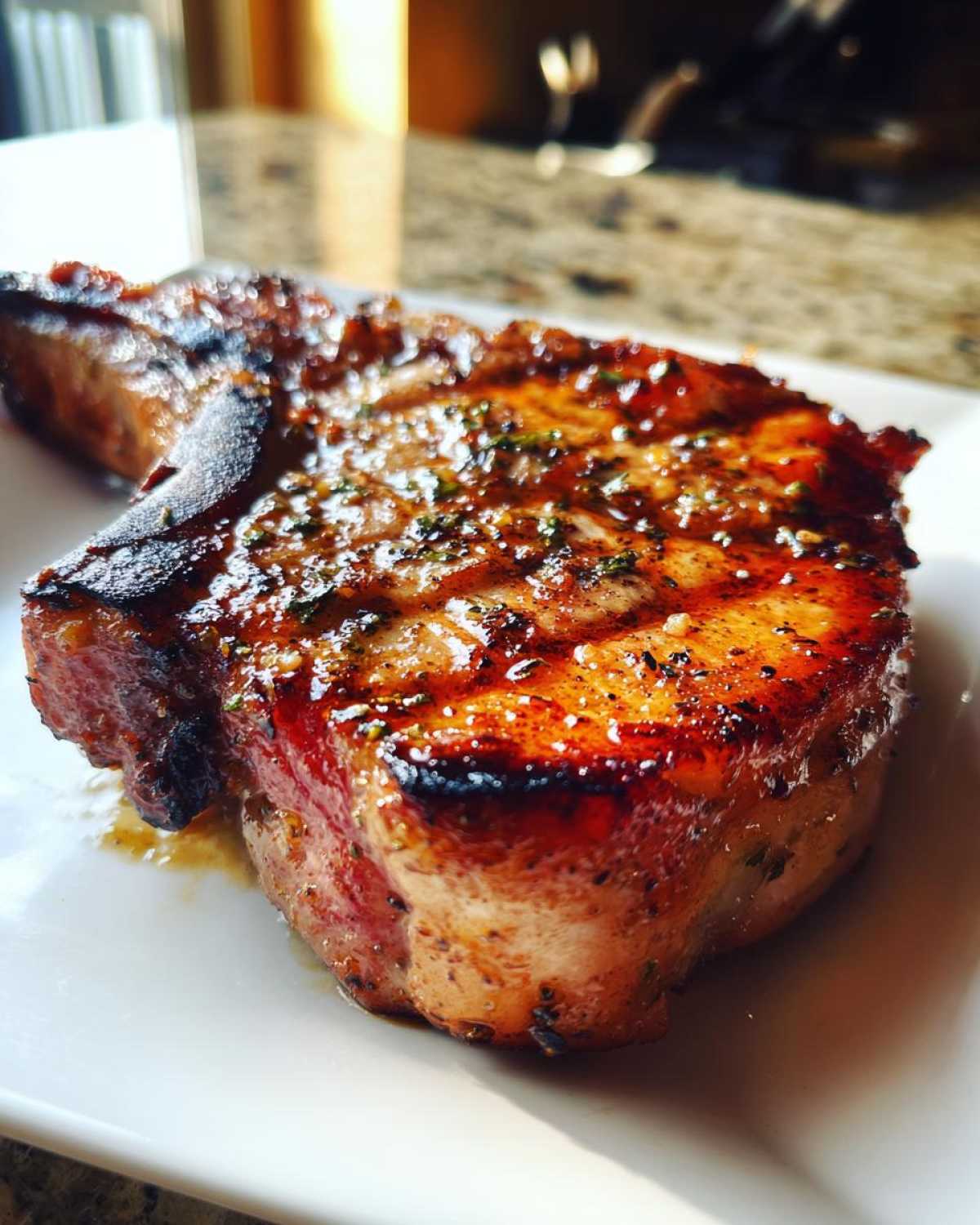 Close-up of a thick, juicy, grilled pork chop glistening with glaze, seasoned with herbs, prepared using a marinade for pork chops.
