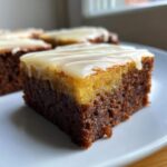 Close-up of a square slice of Lemon Brownies with a rich, dark base and a bright yellow layer topped with white lemon glaze.