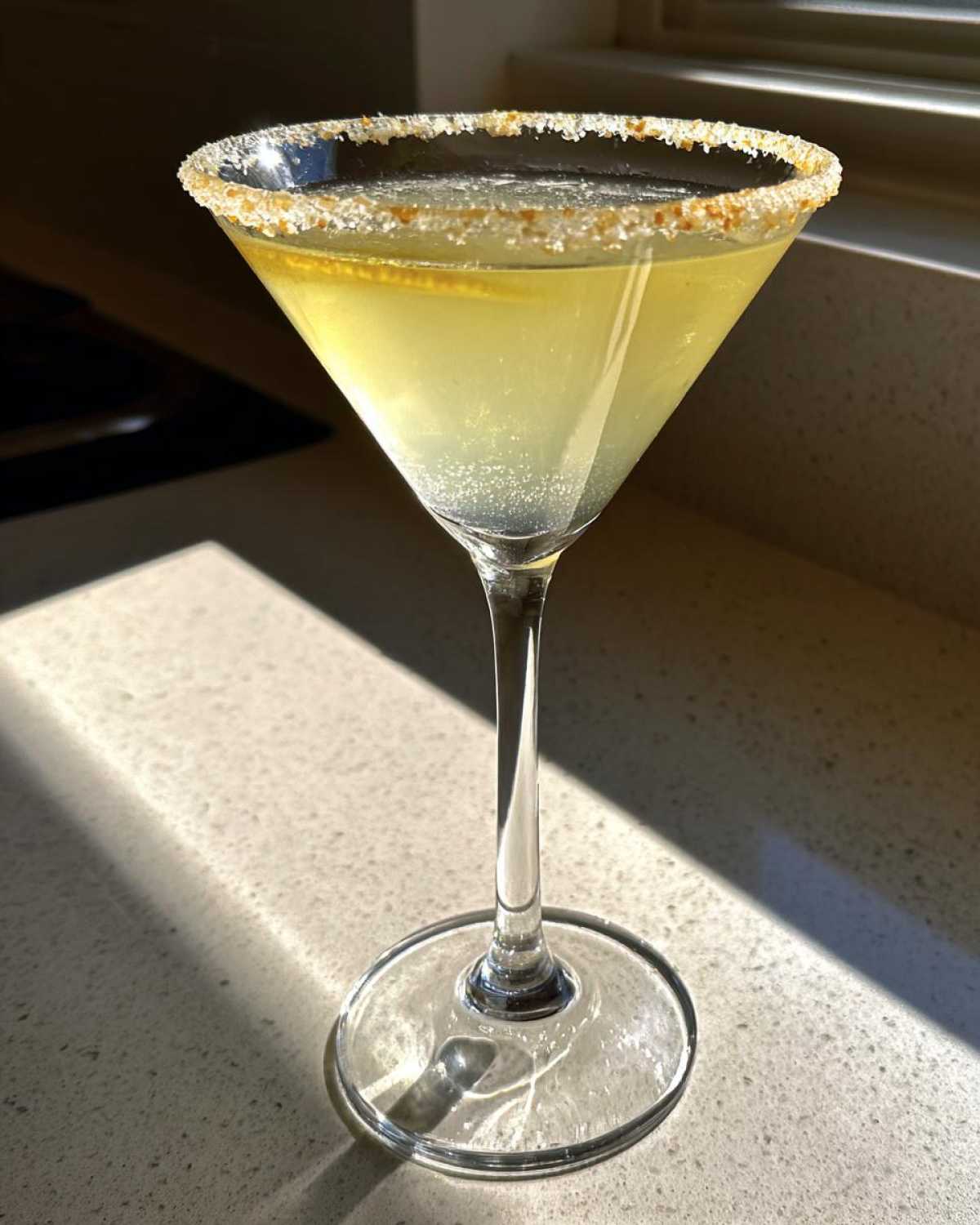 A chilled lemon drop cocktail in a martini glass with a sugar rim, catching bright sunlight.