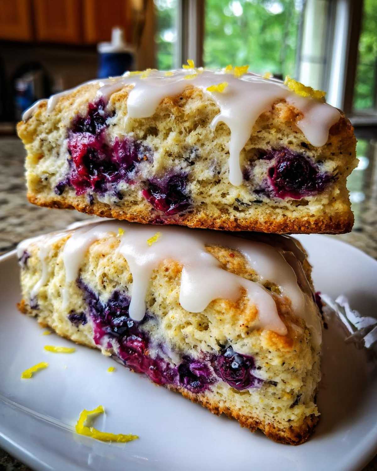 Two halves of a moist blueberry scone stacked, showing juicy berries and a thick lemon glaze.