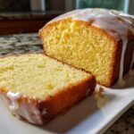 Close-up of a slice cut from a moist lemon pound cake topped with a thick, dripping lemon glaze.