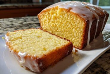 Close-up of a slice cut from a moist lemon pound cake topped with a thick, dripping lemon glaze.