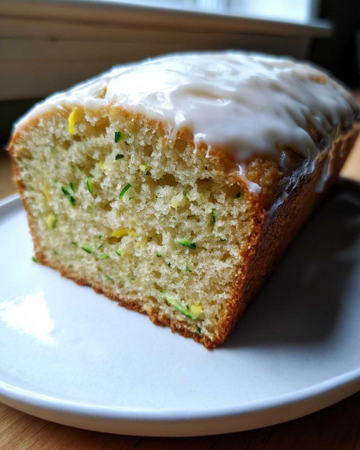 A close-up view of a slice of moist lemon zucchini bread topped with a thick white glaze.