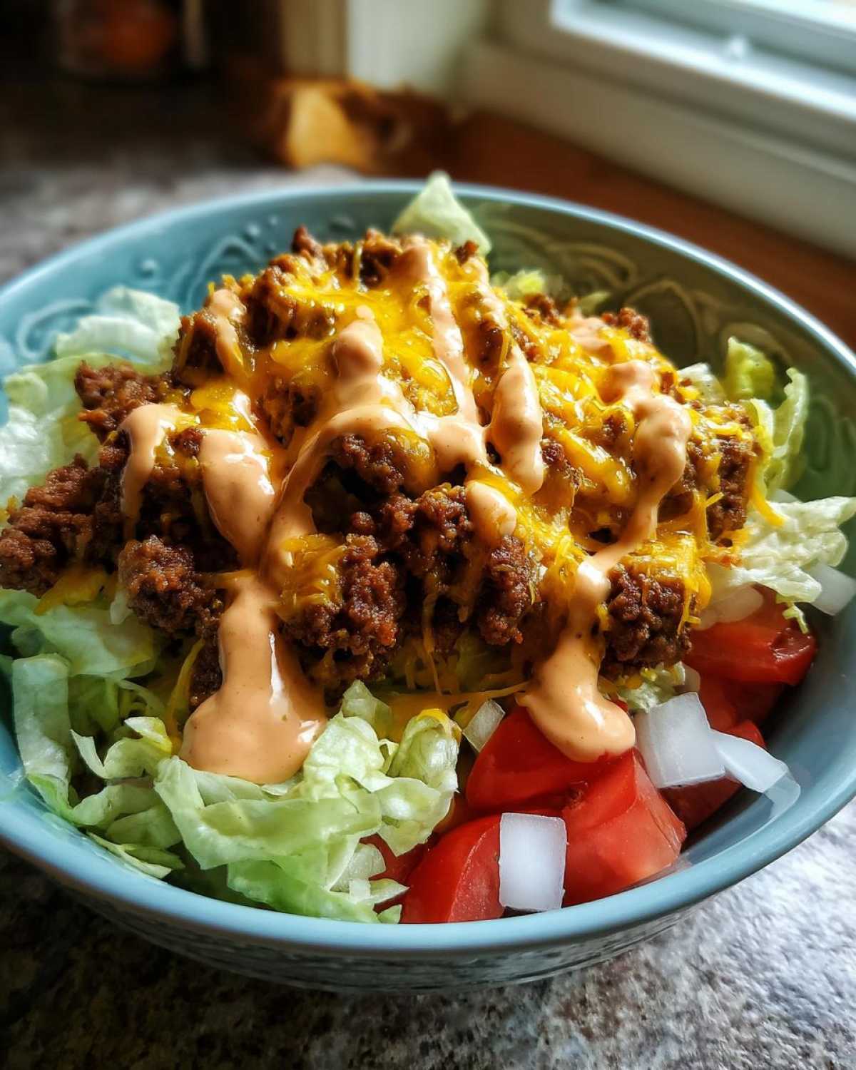 A close-up of a delicious cheeseburger bowl featuring seasoned ground beef, melted cheddar, special sauce, lettuce, tomatoes, and onions.