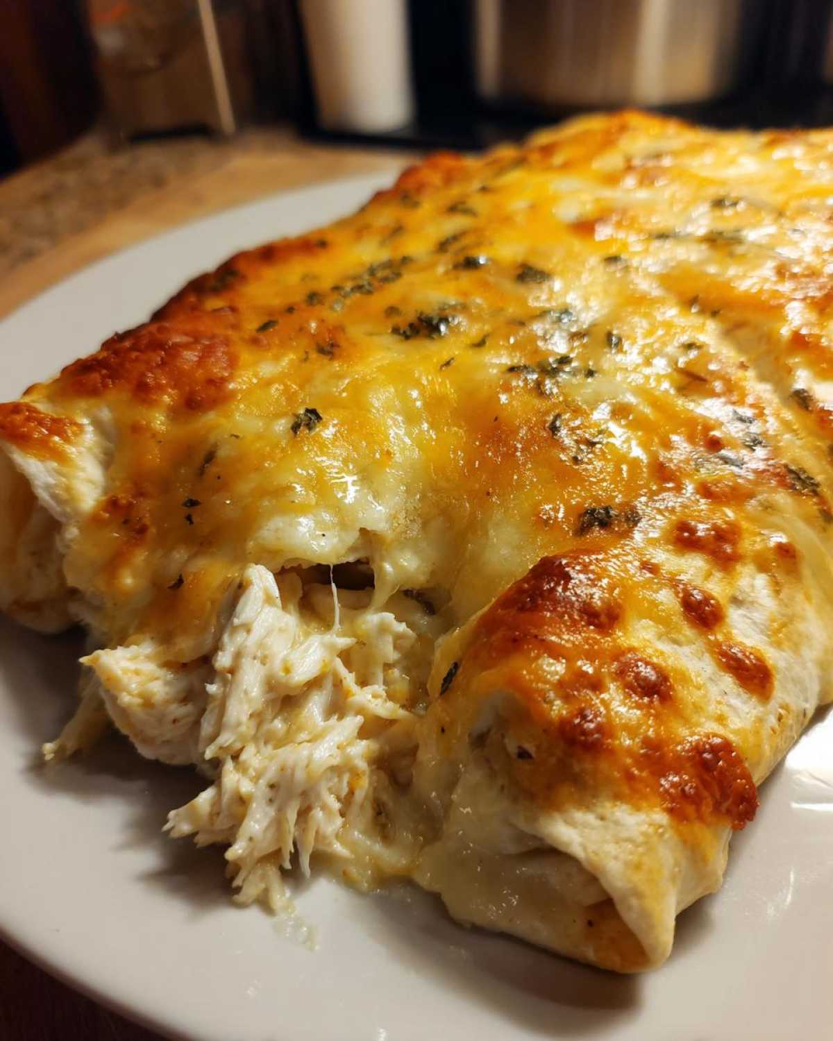 Close-up of cheesy green chile chicken enchiladas, showing shredded chicken filling spilling out.