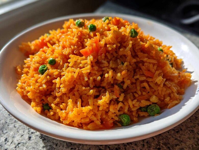 A close-up of a mound of vibrant orange Mexican rice recipe served in a white bowl, garnished with green peas.