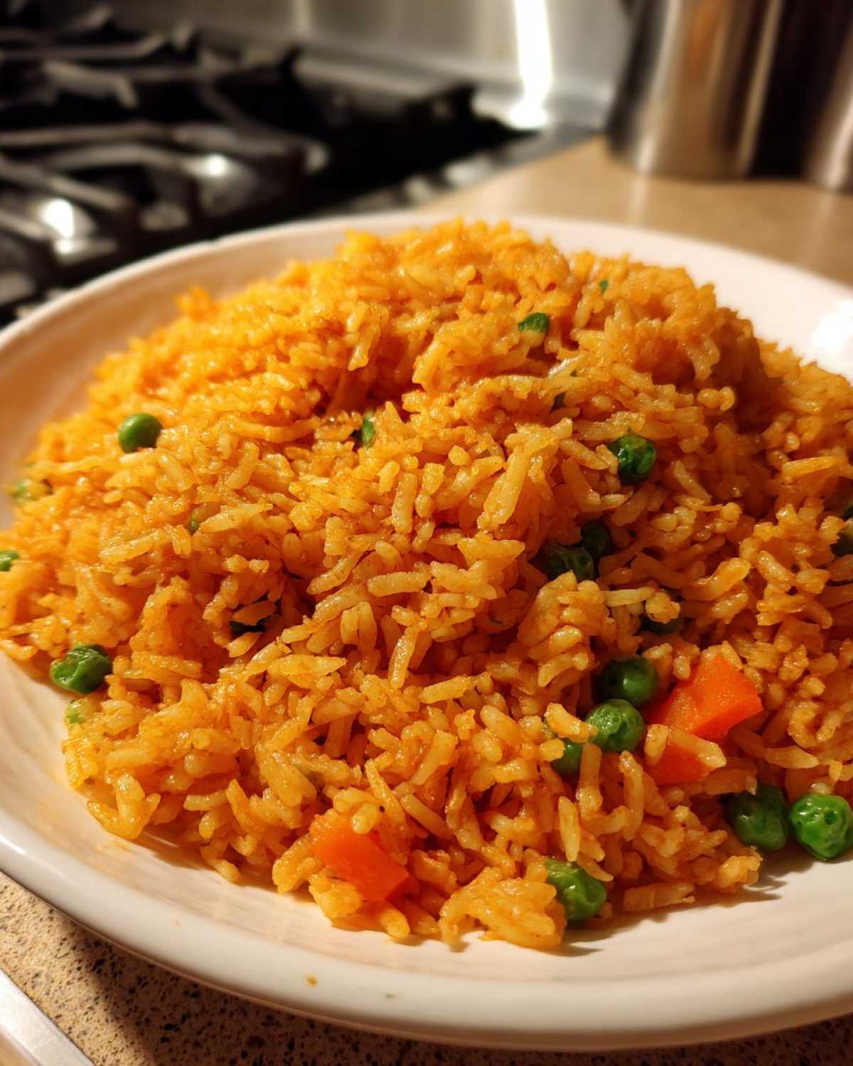 A close-up of a bowl filled with vibrant orange Mexican rice recipe mixed with bright green peas and diced carrots.