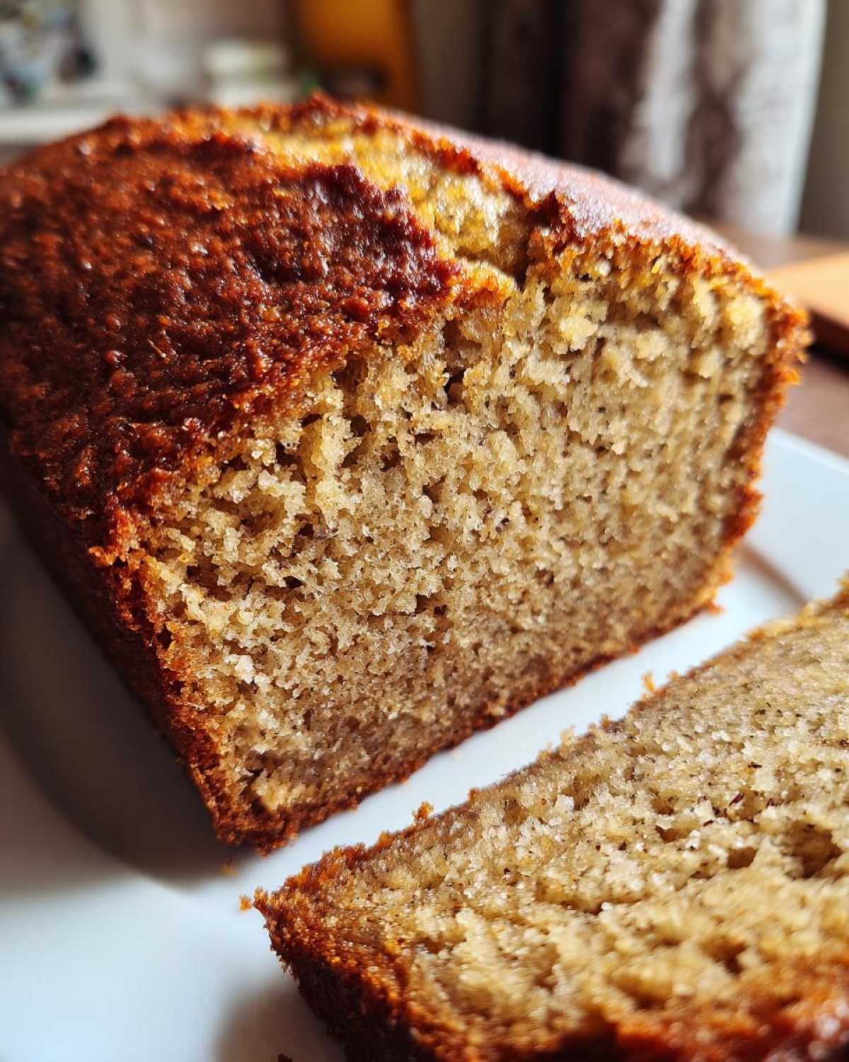 Close-up of a moist banana bread loaf, showing the rich brown crust and soft, textured interior.