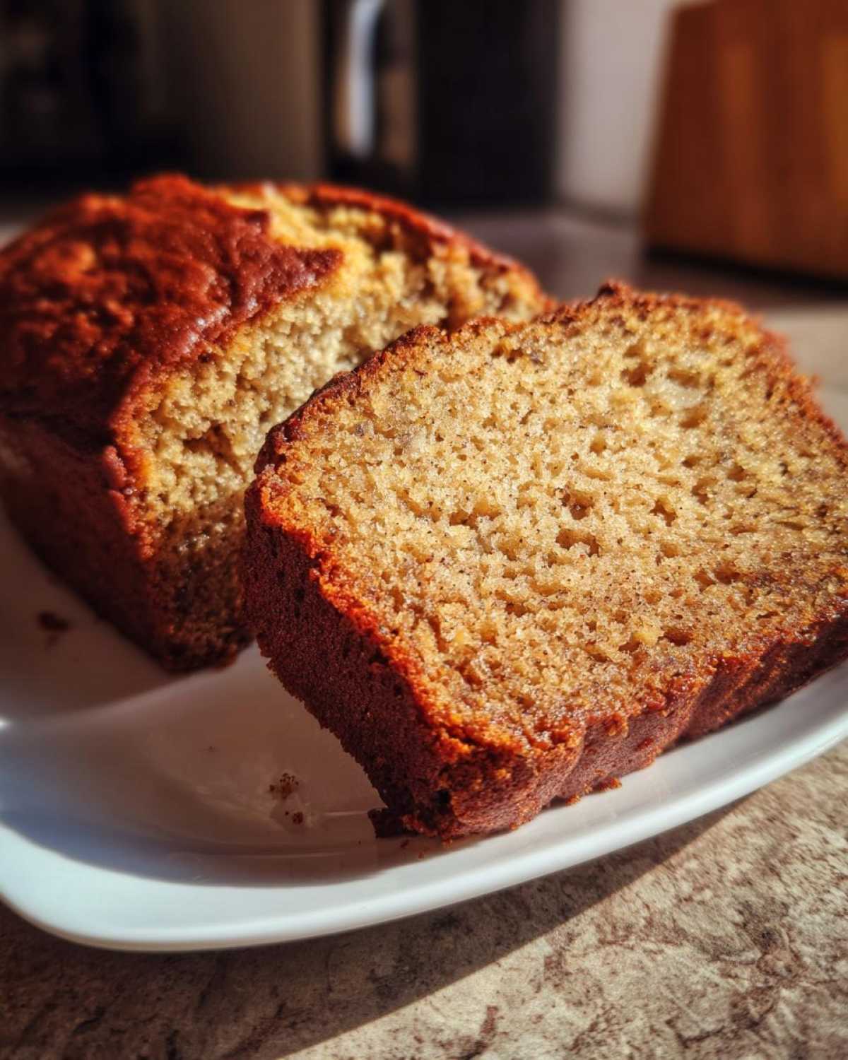 Close-up of two slices of moist banana bread with a dark, caramelized crust on a white plate.