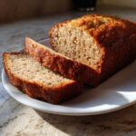 A loaf of moist banana bread with two slices cut, resting on a white plate.