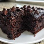 Two rich, dark slices of moist black bean brownies topped with melted chocolate chips on a white plate.