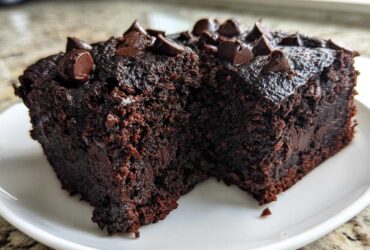 Two rich, dark slices of moist black bean brownies topped with melted chocolate chips on a white plate.