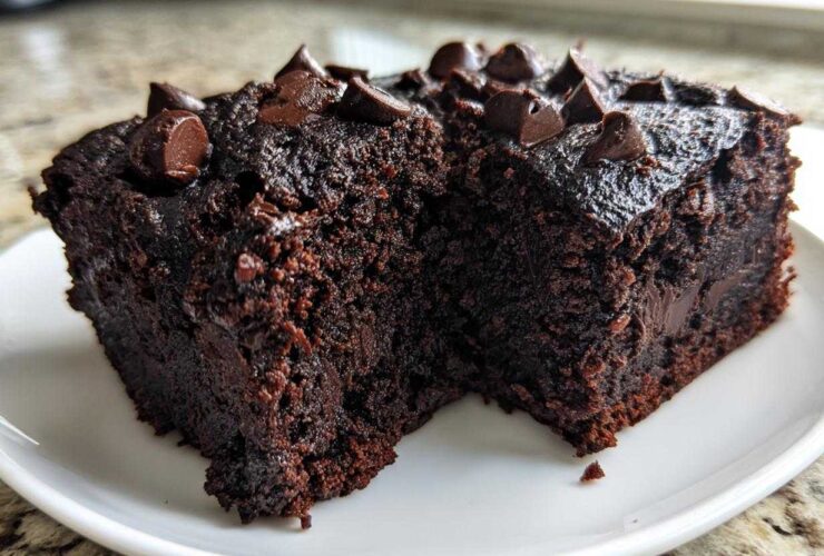 Two rich, dark slices of moist black bean brownies topped with melted chocolate chips on a white plate.