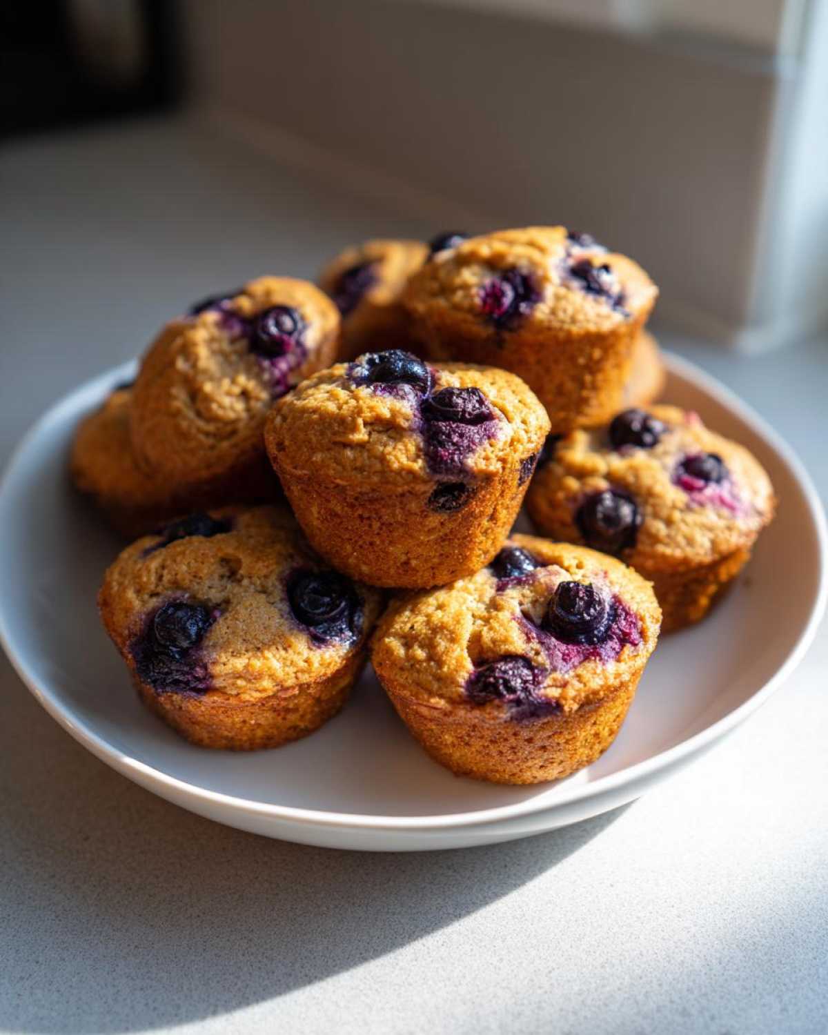 A stack of golden brown blueberry protein muffins with visible blueberries on top, sitting on a white plate.