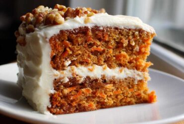 Close-up of a moist, two-layer carrot cake recipe slice with thick cream cheese frosting and chopped walnuts.